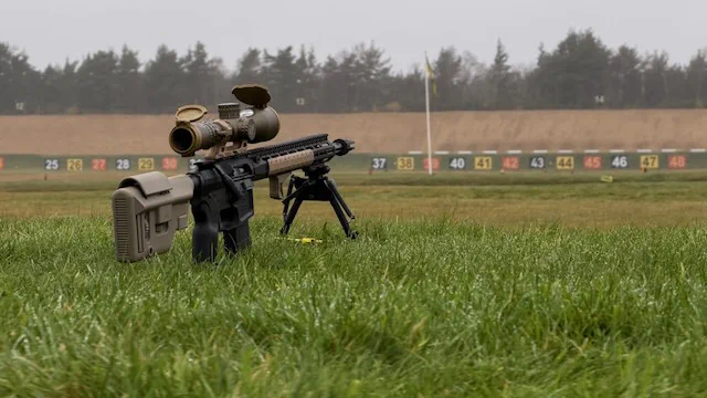 A straight-pull service rifle on the firing point at Bisley, the numbered target butts and range flag behind