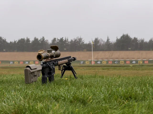 A straight-pull service rifle on the firing point at Bisley, the numbered target butts and range flag behind